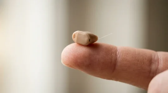 Gros plan d'un minuscule appareil auditif intra-auriculaire CIC posé délicatement sur un doigt, illustrant sa taille discrète